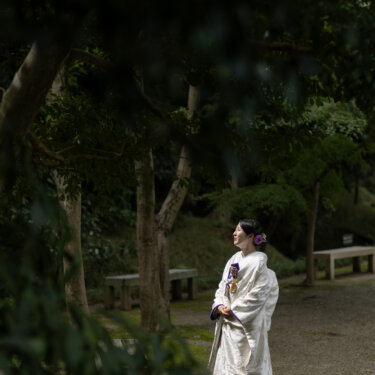 深い木立の中の小道にたたずみ、振り返るように遠くを見る白無垢の花嫁。日本庭園で撮る和装フォトウェディング