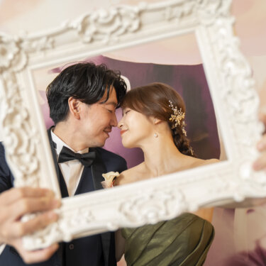 白い額縁の中でおでこを寄せ合うネイビーのタキシードの新郎と花の髪飾りの花嫁。東京駅店のスタジオフォトで人気の額縁ポーズ