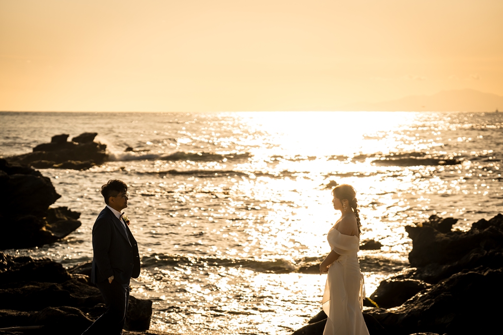 夕日にきらめく城ヶ島の海の前で、向かい合う新郎新婦のシルエット