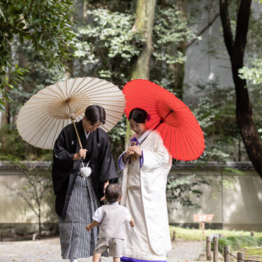 白と赤の和傘を差して石畳に立つ紋付袴の新郎と白無垢の花嫁、そこへ歩み寄る男の子。家族で撮る和装前撮り