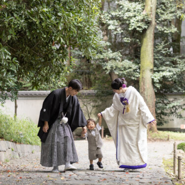 白壁沿いの石畳の小道で、よちよち歩く男の子の手を引く紋付袴の新郎と白無垢の花嫁。小石川後楽園の和装前撮り