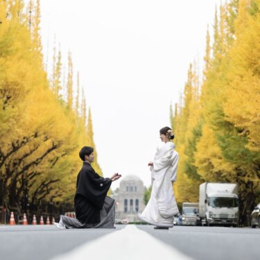 外苑いちょう並木の道で、ひざまずいてプロポーズを再現する紋付袴の新郎と白無垢の花嫁
