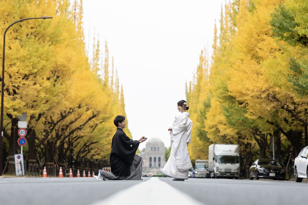 外苑いちょう並木の道で、ひざまずいてプロポーズを再現する紋付袴の新郎と白無垢の花嫁