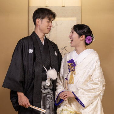 掛け軸の前で白いブーケを持つ白無垢の花嫁と、照れて目をそらす紋付袴の新郎。和室で撮る結婚写真