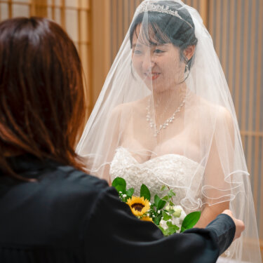 ベール越しにはにかむティアラの花嫁と、ひまわりのブーケ。ベールダウンの瞬間を収めたチャペルでの結婚写真