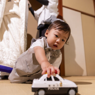 白無垢と紋付袴の両親の足元で、パトカーのおもちゃを走らせる男の子。家族で撮る和装前撮りのほほえましい一枚
