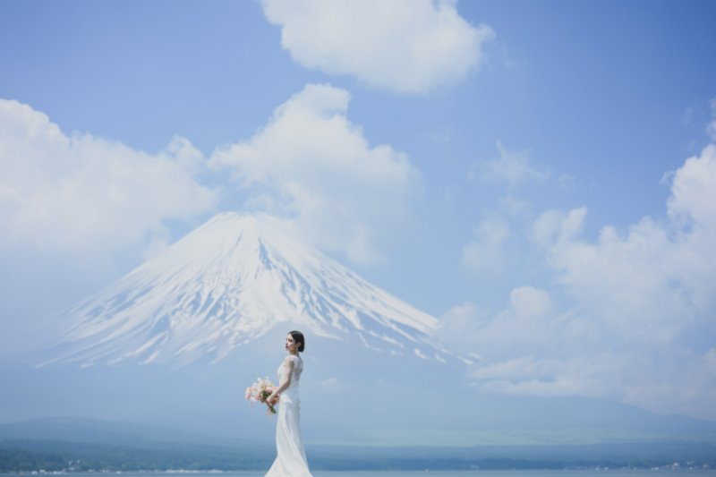 山中湖の湖畔に立つ花嫁と、湖の向こうにそびえる富士山