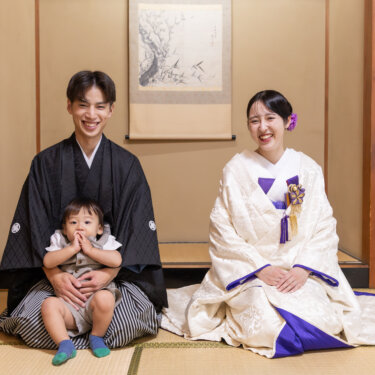 床の間の前の畳に座り、赤ちゃんをひざに乗せた紋付袴の新郎と白無垢の花嫁。親子3人で撮る和装フォトウェディング