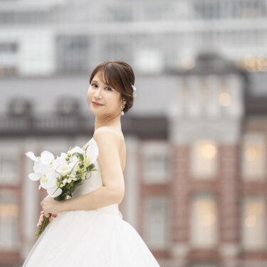 ブーケを手に肩越しに振り返って微笑む、ビスチェのウェディングドレスの花嫁。東京駅丸の内駅舎を背景にした前撮り