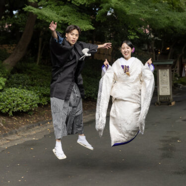 小石川後楽園の木立の小道で、そろって高くジャンプする紋付袴の新郎と白無垢の花嫁。笑顔あふれる和装前撮り