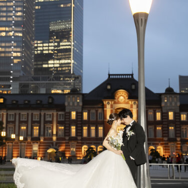 街灯の下でトレーンを広げてキスをする新郎新婦と、ライトアップされた東京駅丸の内駅舎。夜景のフォトウェディング