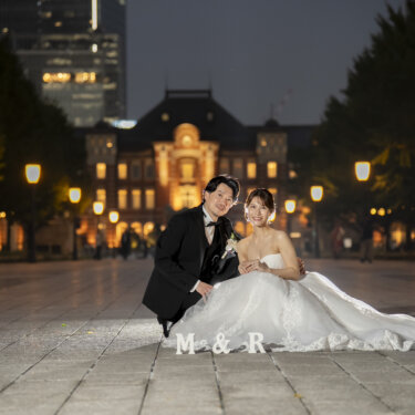 ライトアップされた駅舎へ続く石畳に座り、ドレスを広げて笑う新郎新婦。夜景で撮る洋装前撮り