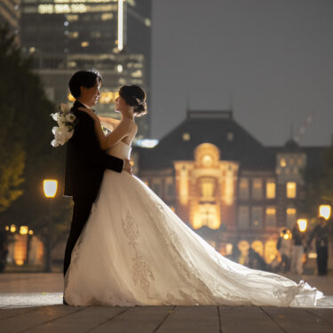 ライトアップされた駅舎の前で抱き合い、トレーンを石畳に広げる新郎新婦のシルエット。夜景のフォトウェディング