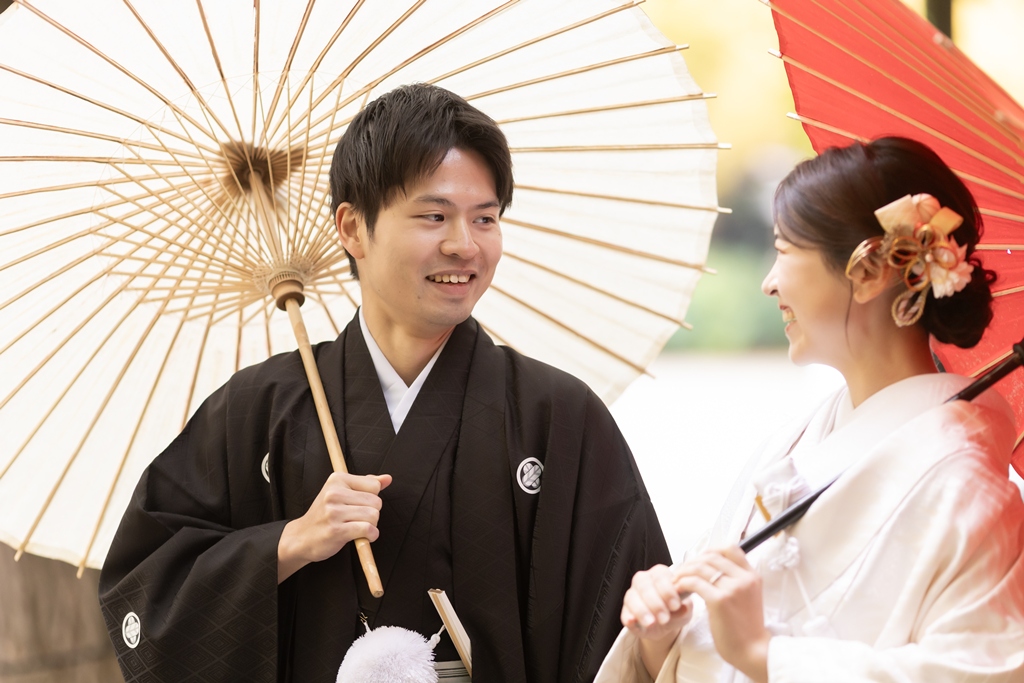 外苑いちょう並木で白と赤の和傘を差して笑い合う白無垢の花嫁と紋付袴の新郎