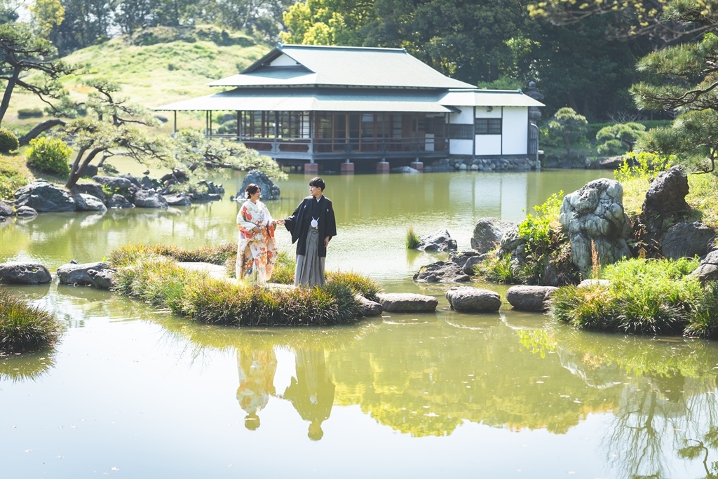 清澄庭園の池に浮かぶように建つお茶室・涼亭と、島の上に立つ和装の新郎新婦。前撮りで人気の撮影スポット